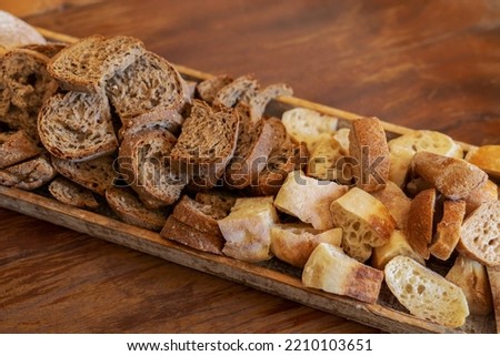 Wooden serving platter piled high with small slices of white sourdough bread and multigrain brown bread, on wooden table Royalty-Free Stock Photo #2210103651