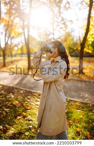 Young woman taking pictures in the autumn forest. Lady Walking In Fall Park With Yellow Foliage.