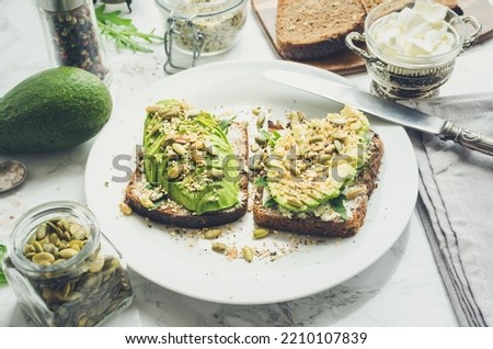 Healthy avocado toasts for breakfast or lunch with rye bread, cream cheese, arugula, sliced avocado, pumpkin, hemp and sesame seeds, salt and pepper. Vegetarian sandwiches. Clean eating.