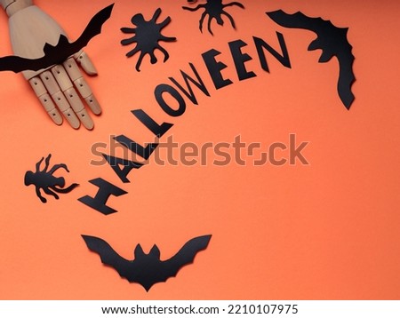 Halloween concept with artificial arm, bats and spiders on orange background. Halloween lettering with a wooden hand and figures of bats. Copy space
