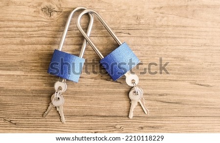Two metal closed blue locks with inserted keys on a wooden background