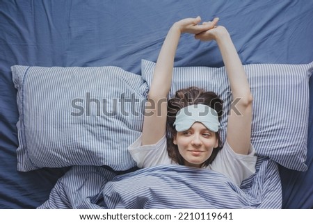 top view of a woman in bed wearing a sleep mask, a happy European woman wakes up and stretches, does a warm-up, insomnia and sleep deprivation. the woman has had a good night's sleep and is resting Royalty-Free Stock Photo #2210119641