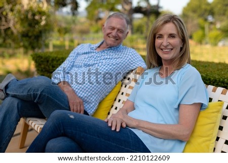 Front view of a senior Caucasian couple in the garden, sitting on chairs relaxing and smiling to camera. Home and lifestyle weekend activities.