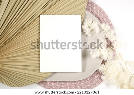 Scandinavian Boho Theme Product Mockup. Blank greeting card, party invitation flatlay styled with bohemian theme dried palm frond leaf and natural materials against a white background.