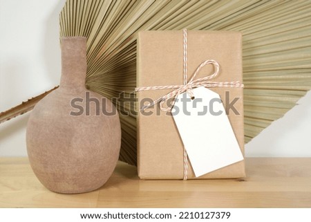 Scandinavian Boho Theme Product Mockup. Gift tag mock up with beige ceramic vase and dried palm frond leaf against a white wall background.