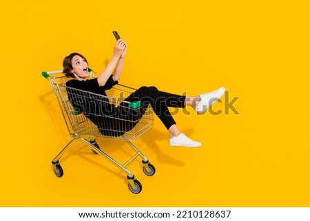 Photo of funky pretty girl dressed formal shirt riding shopping tray recording self video vlog empty space isolated yellow color background