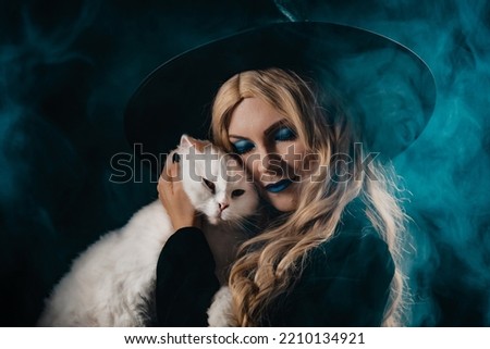 Pretty witch with white furry magic cat on dark background. Happy Halloween, masquerade costume, trick or treat, classic hag. High quality photo
