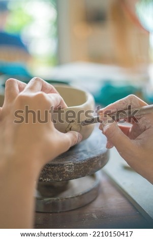 Woman potter working on potters wheel making ceramic pot from clay in pottery workshop. art concept. Focus hand young woman attaching clay product part to future ceramic product. Pottery workshop.