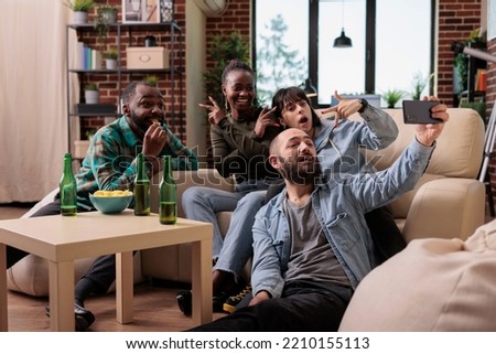 Cheerful group of people taking pictures with smartphone at house party, celebrating friendship event with drinks. People making memories with fun photos and selfies, leisure activity.