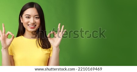 Everything under control. Friendly pleasant relaxed asian girl keep calm, assure all good, show okay ok sign, smiling approval, accept excellent idea, stand green background upbeat delighted quality