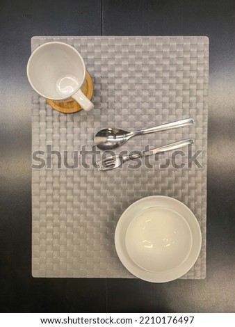 aesthetic close up shot of white ceramic bowl and plate, ceramic white cup with wooden plate, metallic spoon and fork placed on synthetic grey woven texture table cloth for interior photography ideas