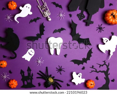 White tooth with Halloween decorations on purple background. Dentist Halloween concept. Top view, flat lay.
