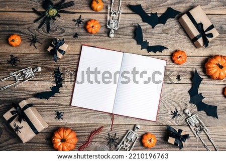 Open empty diary surrounded by Halloween decorations on a wooden table. Top view rustic background with copy space.