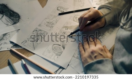 Young female artist draws sketches of comic book characters on a sheet of paper. The illustrator creates a storyboard. Storytelling concept. Video editing. Royalty-Free Stock Photo #2210197335