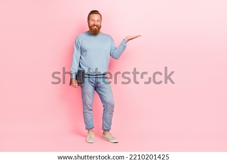 Full size photo of handsome positive guy arm palm hold demonstrate empty space isolated on pink color background