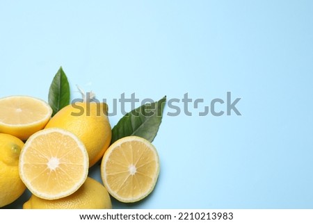 Many fresh ripe lemons with green leaves and flower on light blue background, flat lay. Space for text