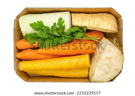 Fresh winter soup pack, uncut and prepacked, in a cardboard tray, from above, isolated over white. Orange and yellow carrots, a quarter of a celery root and of a parsnip, a piece of leek, and parsley. Royalty-Free Stock Photo #2210229557