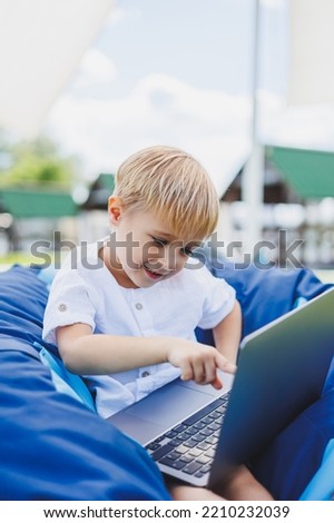A cheerful child is playing on colorful beanbag chairs on the street. A little boy watches cartoons on a laptop while sitting on a chair in the park