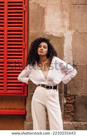 Beautiful young african girl with wavy hair looking at camera posing on street. Woman brunette hair wears classic style of clothes. Concept fashion, beauty.