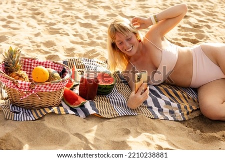 Cheerful young woman enjoy at tropical sand beach. Young woman taking a picture of fruit on the beach.