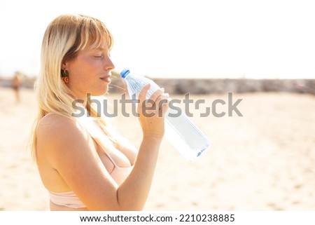 Beautiful woman drinks water. Young happy woman at the beach..	