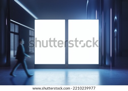 Walking businessman by blank white illuminated screens with place for your logo or text with glossy floor on dark empty room background, mock up Royalty-Free Stock Photo #2210239977
