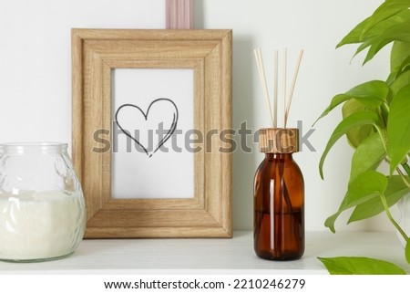 Aromatic reed air freshener, candle and wooden frame on white shelf indoors