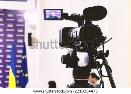 Video camera on a tripod at a press conference.
