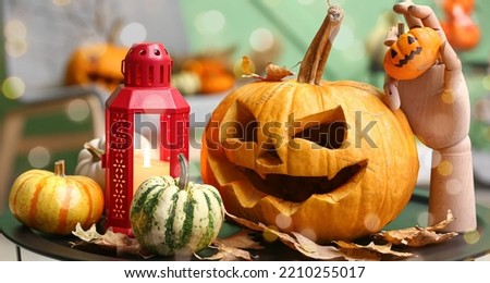 Halloween pumpkins with lantern, autumn leaves and wooden hand on table in living room