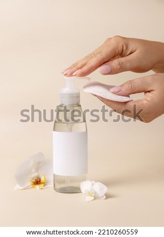 A woman hand pumping liquid on a make-up remover pad from a cosmetic bottle near orchid flowers on beige close up, label mockup. Skincare beauty product package, minimal composition

 Royalty-Free Stock Photo #2210260559
