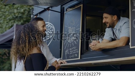 Cheerful waiter taking order from multi-racial customers at counter, Mexican street food served from a food truck