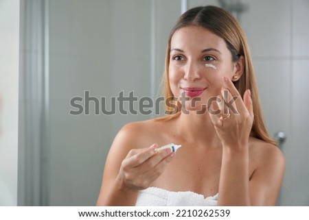 Skin care routine. Portrait of beautiful girl applying cream under eye with finger. Dark circles and anti-wrinkle concept. Royalty-Free Stock Photo #2210262539