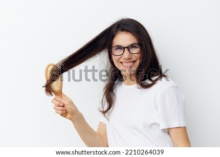 a beautiful, attractive brunette in glasses combs her long hair with a wooden massage comb and screams in pain. Horizontal photo of nc light background with empty space for advertising layout