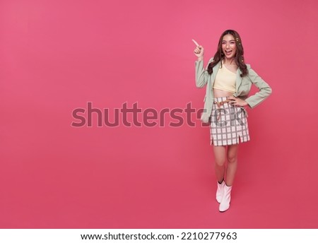 Happy young Asian teen woman standing with her finger pointing empty space isolated on pink background with copy space.