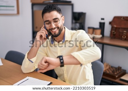 Young arab man business worker talking on smartphone looking watch at office Royalty-Free Stock Photo #2210303519