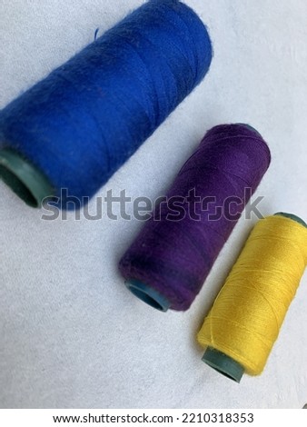 Sewing threads in yellow, purple and blue colors on a white background