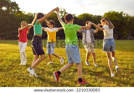 Group of kids playing games and having fun in nature. Joyful little children dancing a round dance on green grass in the park. Several happy little friends holding hands and running in a circle