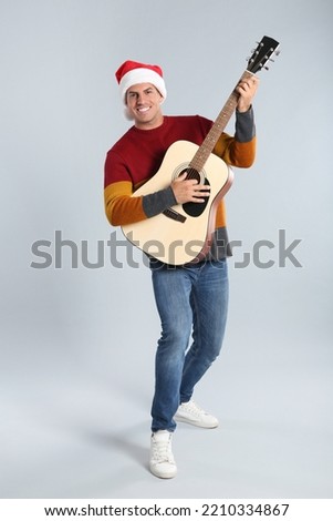 Man in Santa hat playing acoustic guitar on light grey background. Christmas music