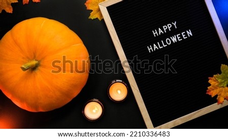 Pumpkin, burning candles, autumn leaves and the inscription Happy Halloween in a wooden frame on a black background