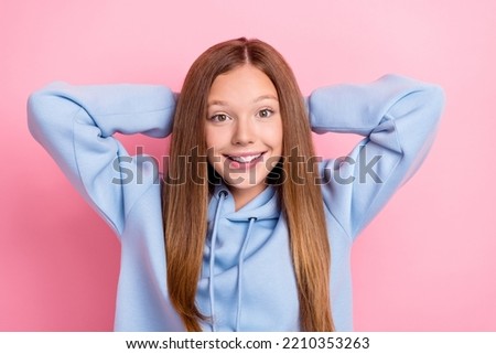 Photo of young pretty little cute positive toothy girl wear blue hoodie touch nape long hair holidays weekend rest excited isolated on pink color background