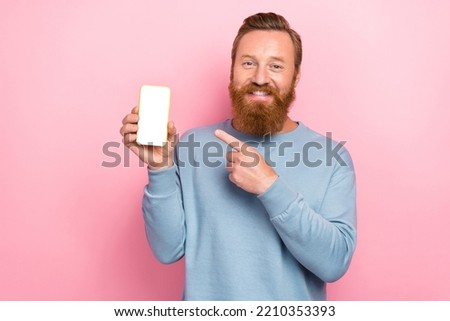 Portrait of satisfied positive red hair guy dressed blue pullover finger demonstrating app in smartphone isolated on pink color background