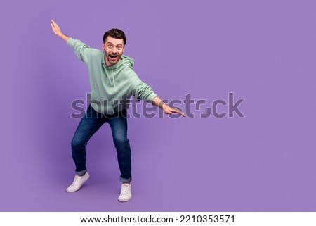 Full size photo of handsome young man spread hands surfing have fun dressed stylish khaki clothes isolated on purple color background