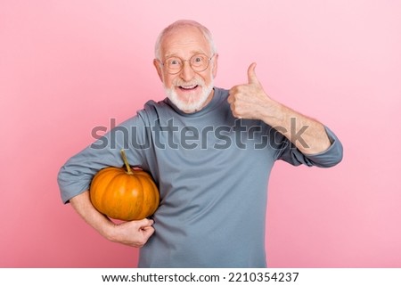 Photo of funky cute guy pensioner dressed grey pullover glasses holding pumpkin thumb up isolated pink color background