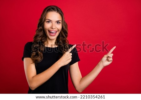 Photo of excited pretty young woman wear black t-shirt pointing two fingers empty space smiling isolated red color background