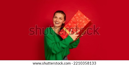 Portrait of smiling happy woman holding big present box isolated over red studio background. Cheerful. Concept of holidays, happiness, emotions, facial expression, joy, celebration