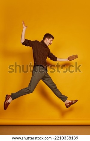 Portrait of young cheerful man jumping in joy with present box isolated over yellow studio background . Happy. Concept of holidays, happiness, emotions, facial expression, joy, celebration