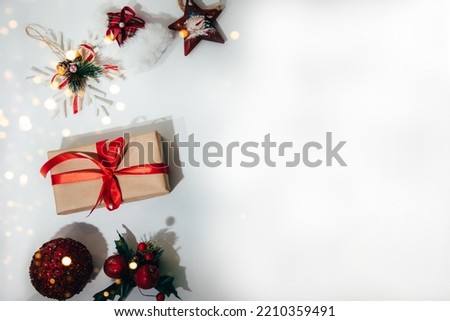 A gift wrapped in brown paper and tied red ribbon with toy star, a red ball and snowflake on a white background. Flat lay