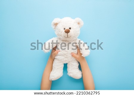 Baby boy hands holding smiling white teddy bear on light blue table background. Pastel color. Closeup. Point of view shot. Kids best friend.  Royalty-Free Stock Photo #2210362795