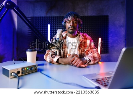 African radio host sitting at desk recording in studio with microphone and laptop