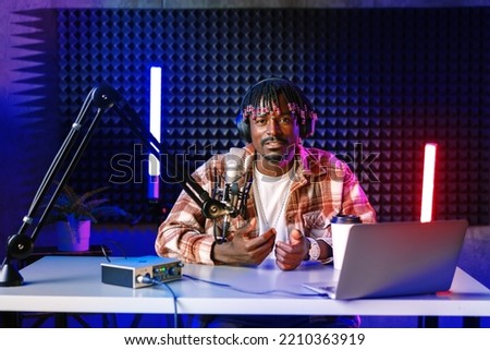 African radio host sitting at desk recording in studio with microphone and laptop